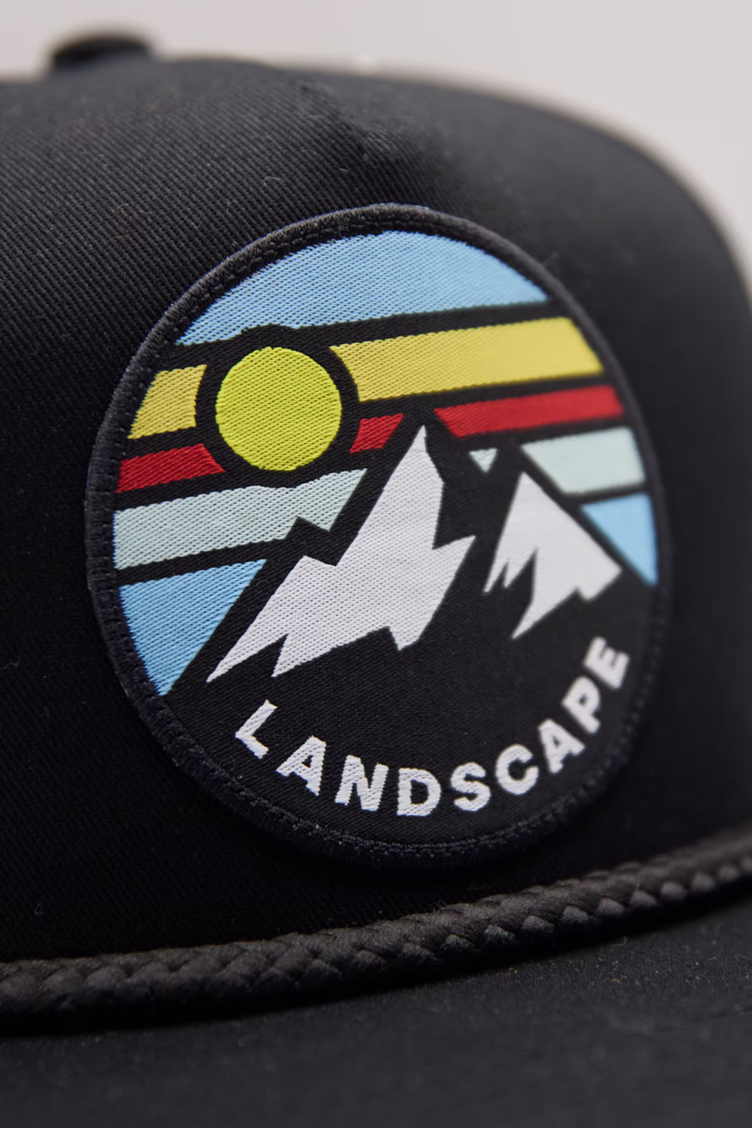 close up a woven patch of a mountain and sun illustration on a black hat