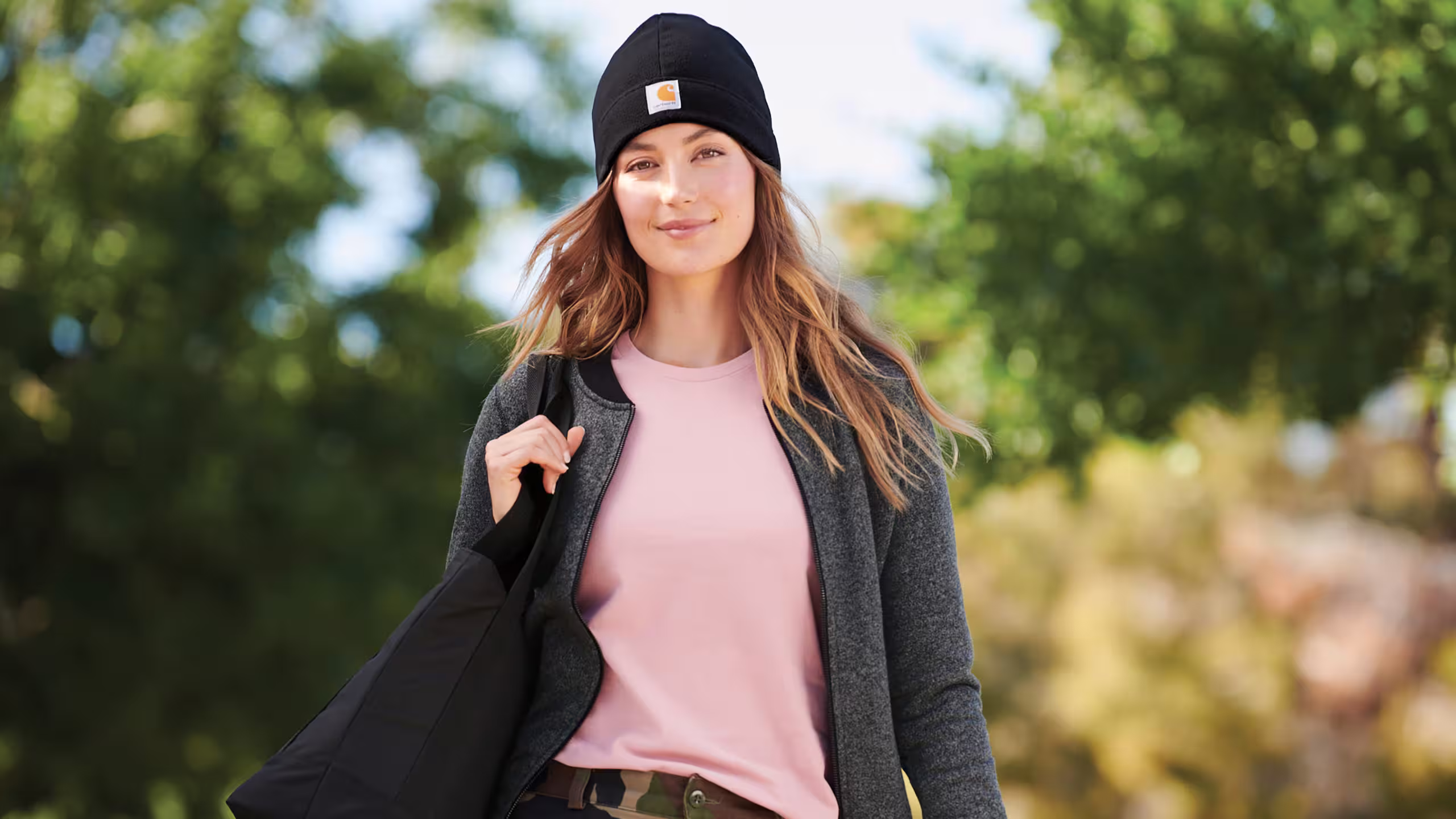 image of a girl wearing a carhartt pink t-shirt, black beanie, and caring a black backpack