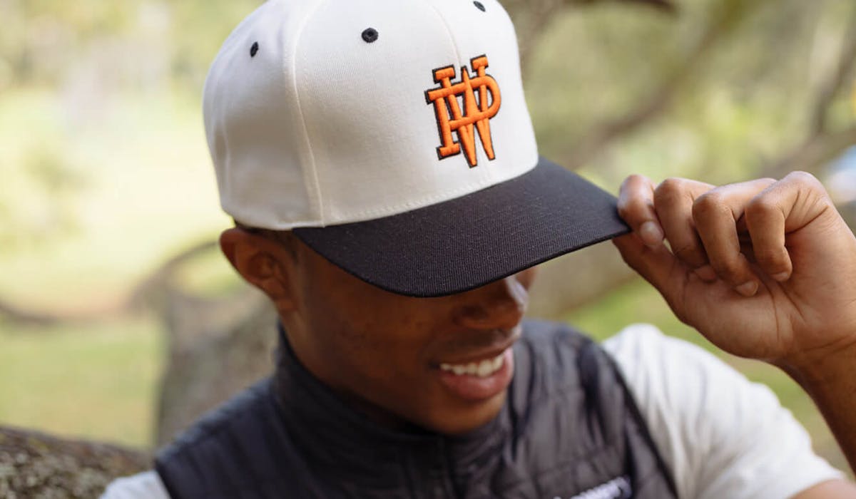man wearing a white and black hat with a orange p. w. monogram embroidered man wearing a white and black hat with a orange p. w. monogram embroidered
