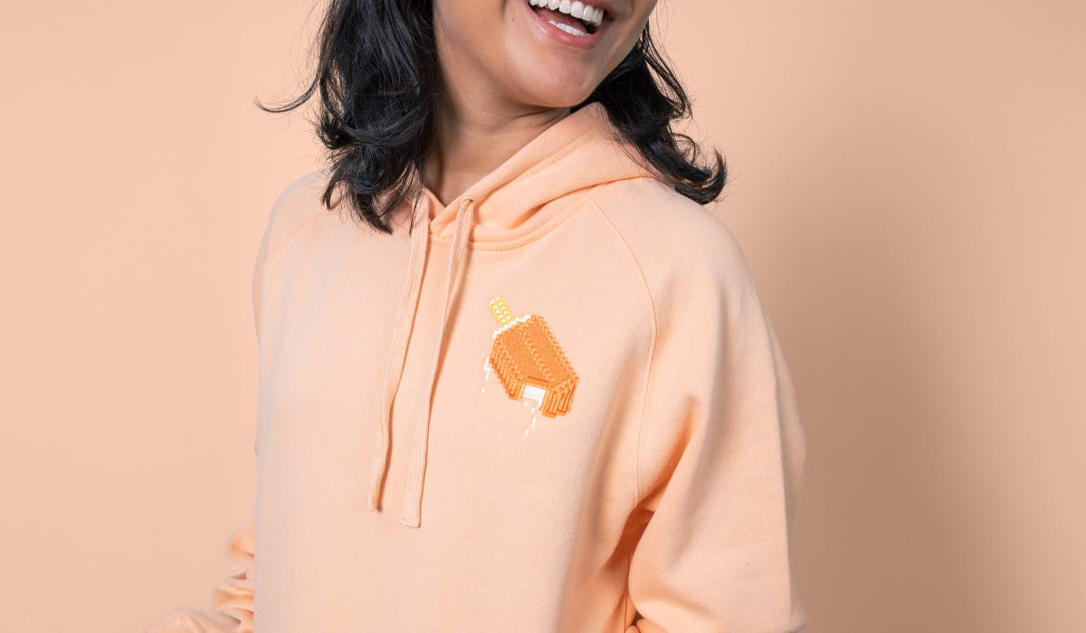 women wearing a peach hoodie with an orange creamsicle embroidered on the top right women wearing a peach hoodie with an orange creamsicle embroidered on the top right